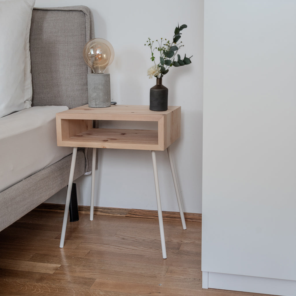 Zirbenholz Nachttisch GREIN neben Bett im Schlafzimmer mit weißen Beinen